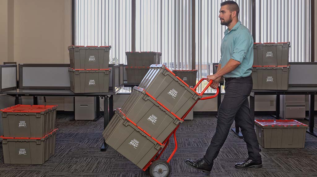 An employee uses a utility dolly to move three U-Haul ready-to-go plastic boxes.