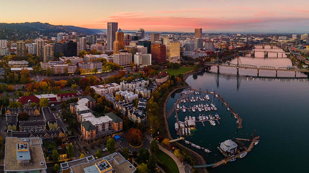 The city of Portland can be seen below in an aerial shot as the sun is setting.
