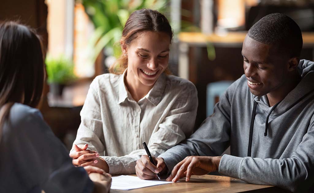 A couple smiles while signing documents with their real estate agent. Housing mortgage rates will remain between 6 to 7 percent in 2024.