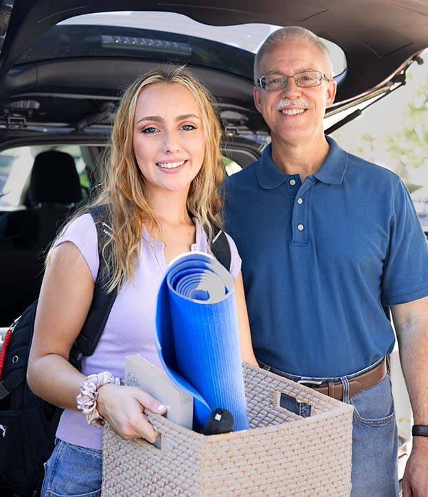 A father and daughter stand next to each other as the daughter unloads her dorm room essentials from her car for school.