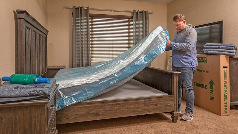 A man lifts his old mattress off his bed. The mattress will be donated or sold.