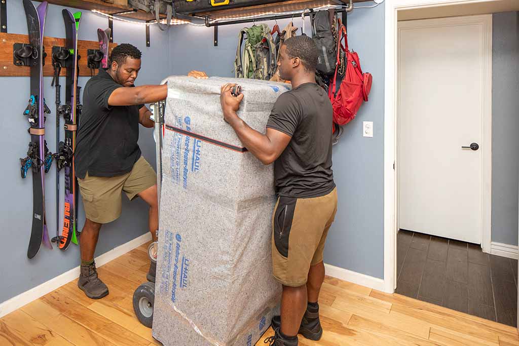 Two Moving Helpers work together to carefully load a customer’s gun safe onto a dolly as they prepare to transport it out of the customer’s home and into the U-Haul truck rental.